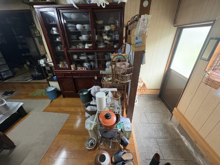 Cluttered kitchen counter with pots, cups, and a metal rack in front of a glass-front china cabinet.