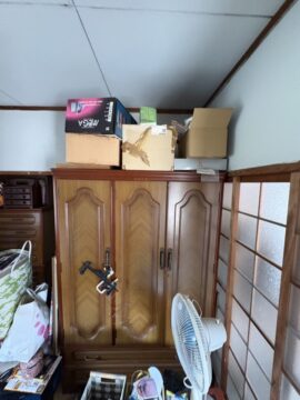 Wooden armoire with several cardboard boxes stacked on top in a cluttered storage area.