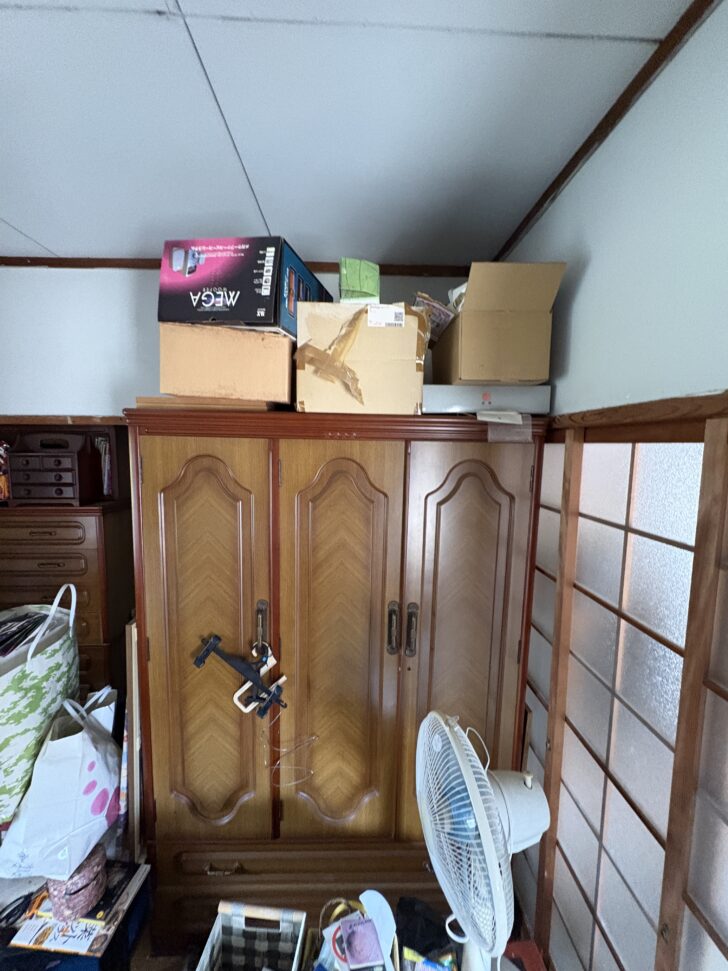 Wooden armoire with several cardboard boxes stacked on top in a cluttered storage area.