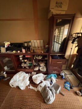 Messy hotel room closet with clothes and miscellaneous items scattered on the floor and dresser shelves.